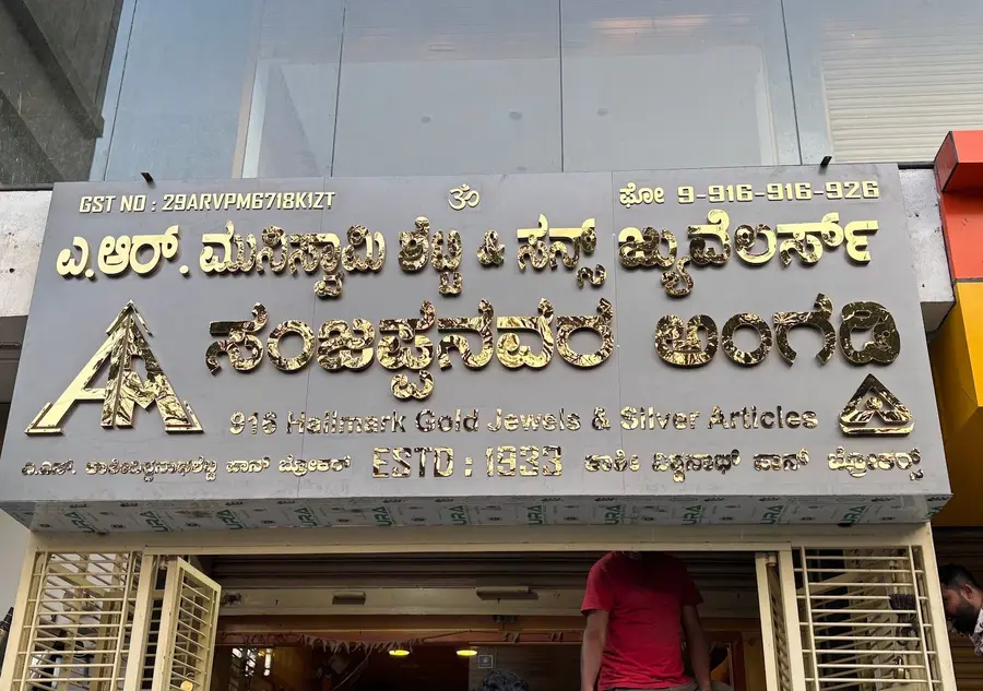 The shop board: the Kannada name with Sanjappa's shop carved beneath it in brass on dark granite, Estd 1953.
